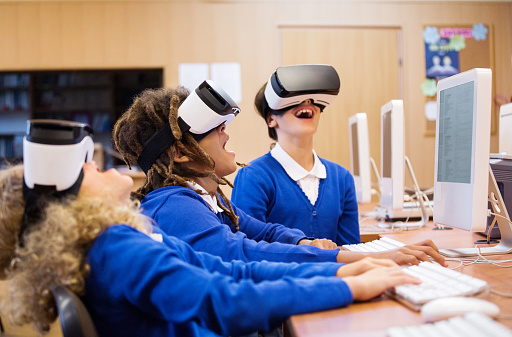 Mixed race group of excited students sitting in a computer lab at school and using virtual reality goggles.